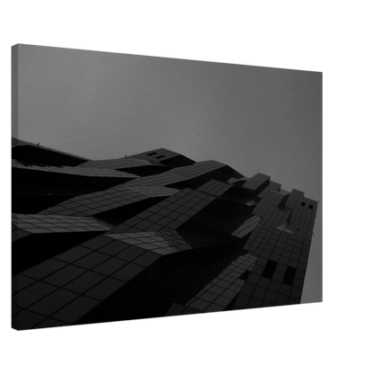 Black and white low angle view of a modern skyscraper with bold geometric lines and dark textured facade on Canvas Print wall art
