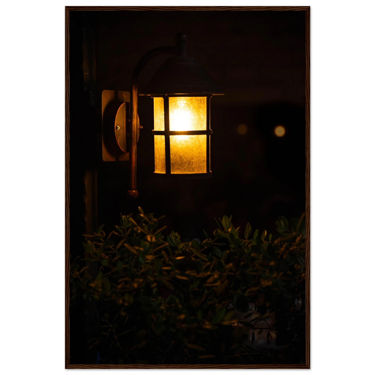 Glowing vintage lantern mounted on a wooden pole in front of a bush at night on wooden framed wall art