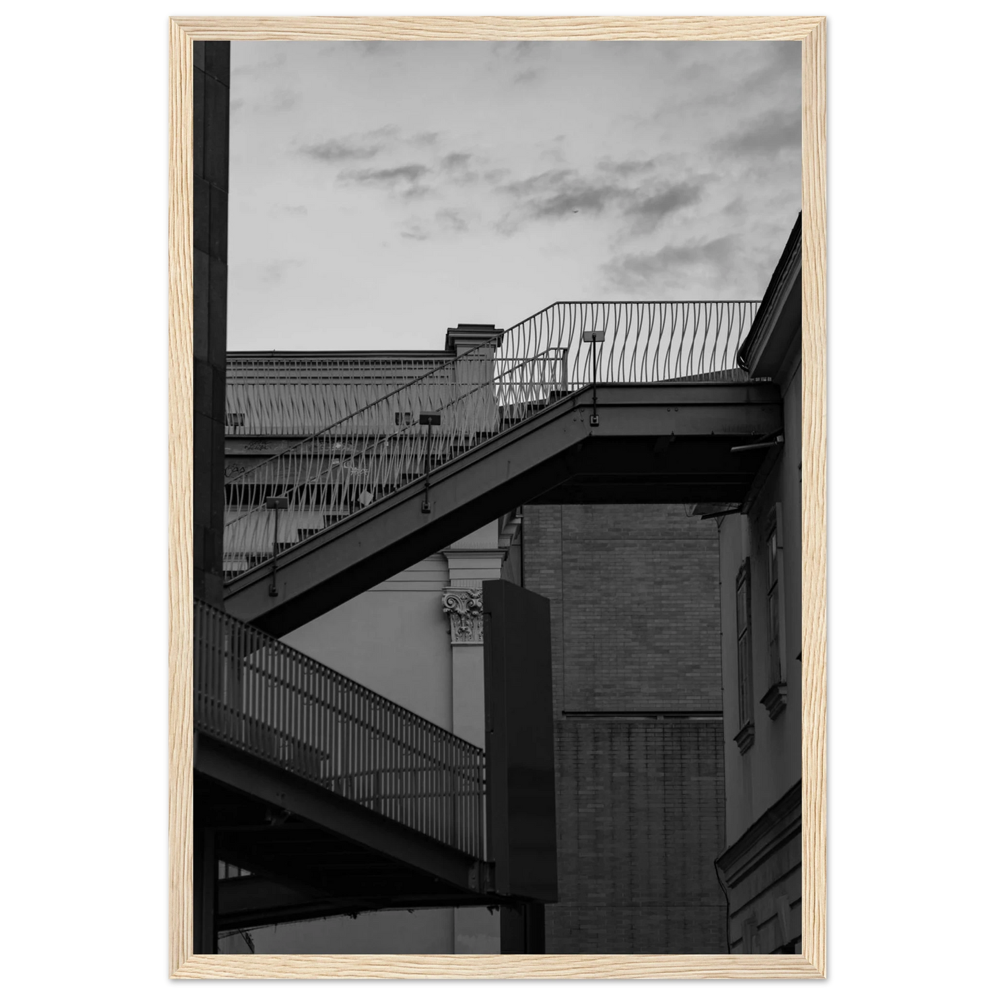 Black and white photo on a wooden frame wall art of an outdoor staircase connecting two buildings under a dramatic cloudy sky