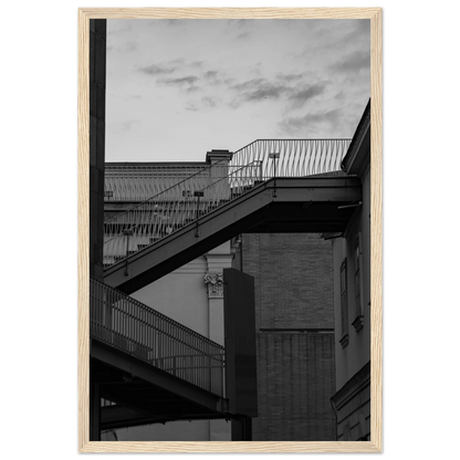 Black and white photo on a wooden frame wall art of an outdoor staircase connecting two buildings under a dramatic cloudy sky