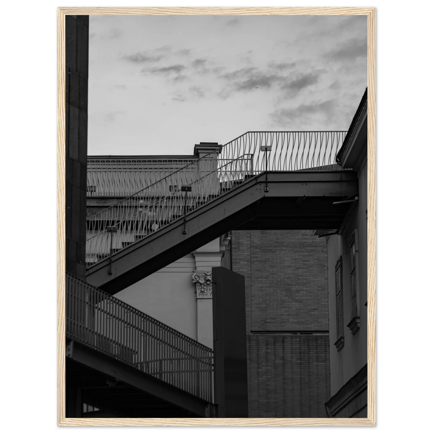 Black and white photo on a wooden frame wall art of an outdoor staircase connecting two buildings under a dramatic cloudy sky