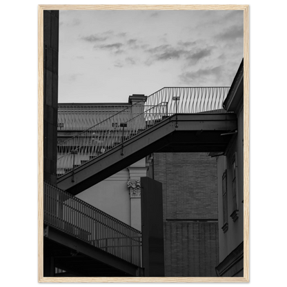 Black and white photo on a wooden frame wall art of an outdoor staircase connecting two buildings under a dramatic cloudy sky