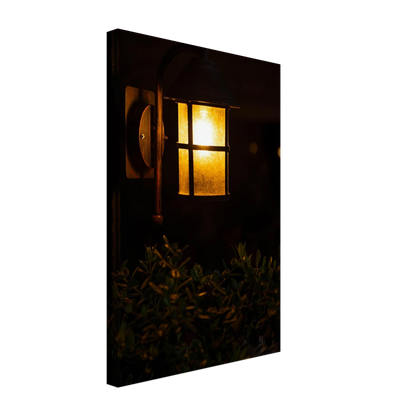 Glowing vintage lantern mounted on a wooden pole in front of a bush at night on Canvas Print wall art