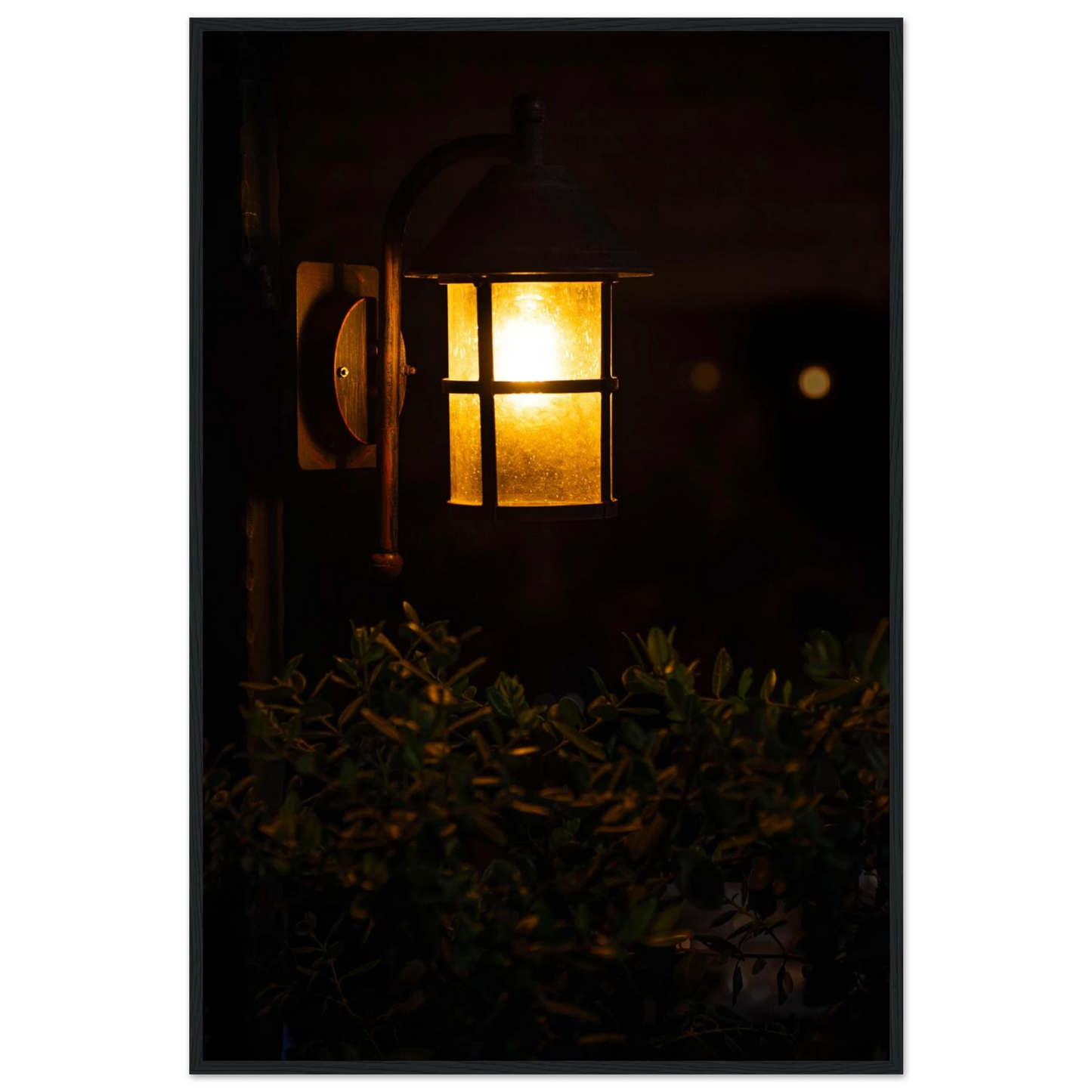 Glowing vintage lantern mounted on a wooden pole in front of a bush at night on wooden framed wall art