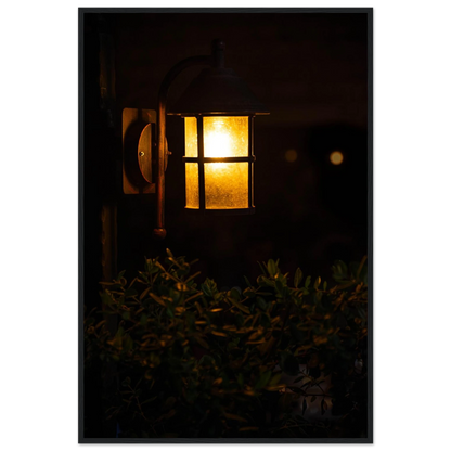 Glowing vintage lantern mounted on a wooden pole in front of a bush at night on wooden framed wall art