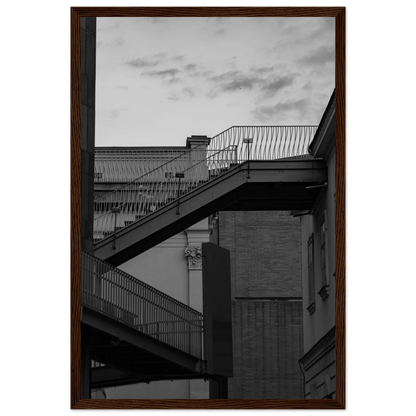 Black and white photo on a wooden frame wall art of an outdoor staircase connecting two buildings under a dramatic cloudy sky