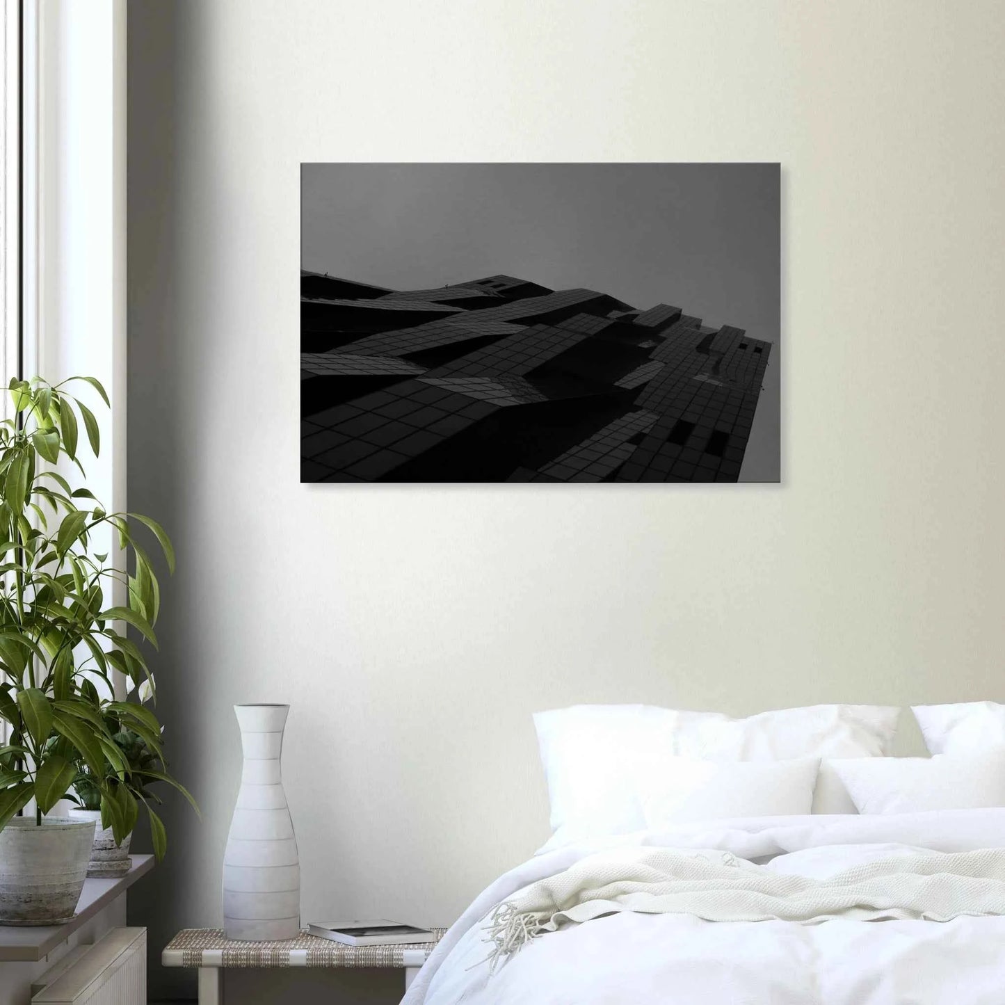 Black and white low angle view of a modern skyscraper with bold geometric lines and dark textured facade on Canvas Print wall art on the wall in the Bedroom
