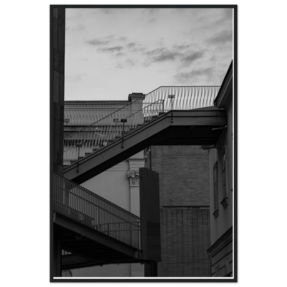 Black and white photo on a wooden frame wall art of an outdoor staircase connecting two buildings under a dramatic cloudy sky