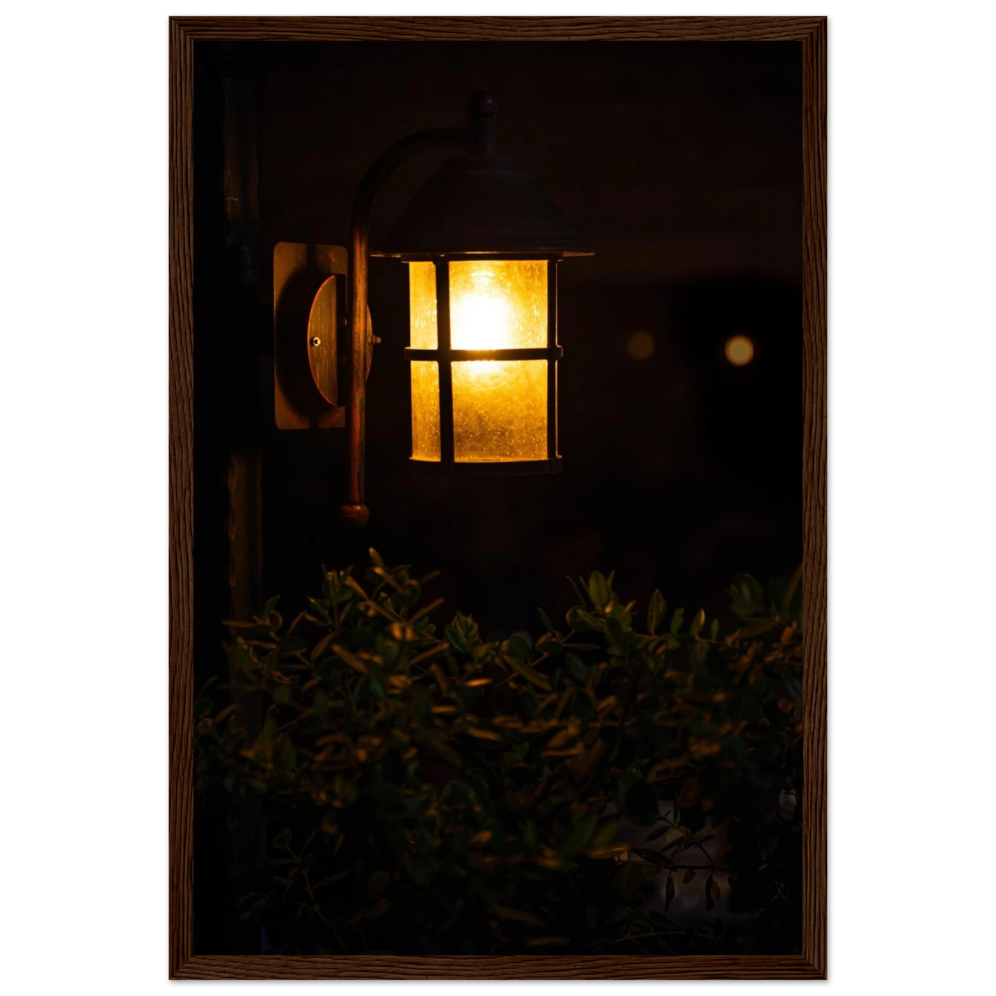 Glowing vintage lantern mounted on a wooden pole in front of a bush at night on wooden framed wall art