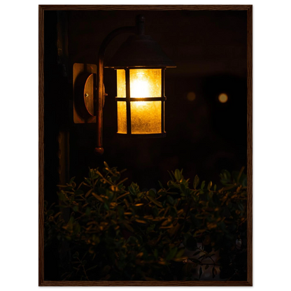 Glowing vintage lantern mounted on a wooden pole in front of a bush at night on wooden framed wall art