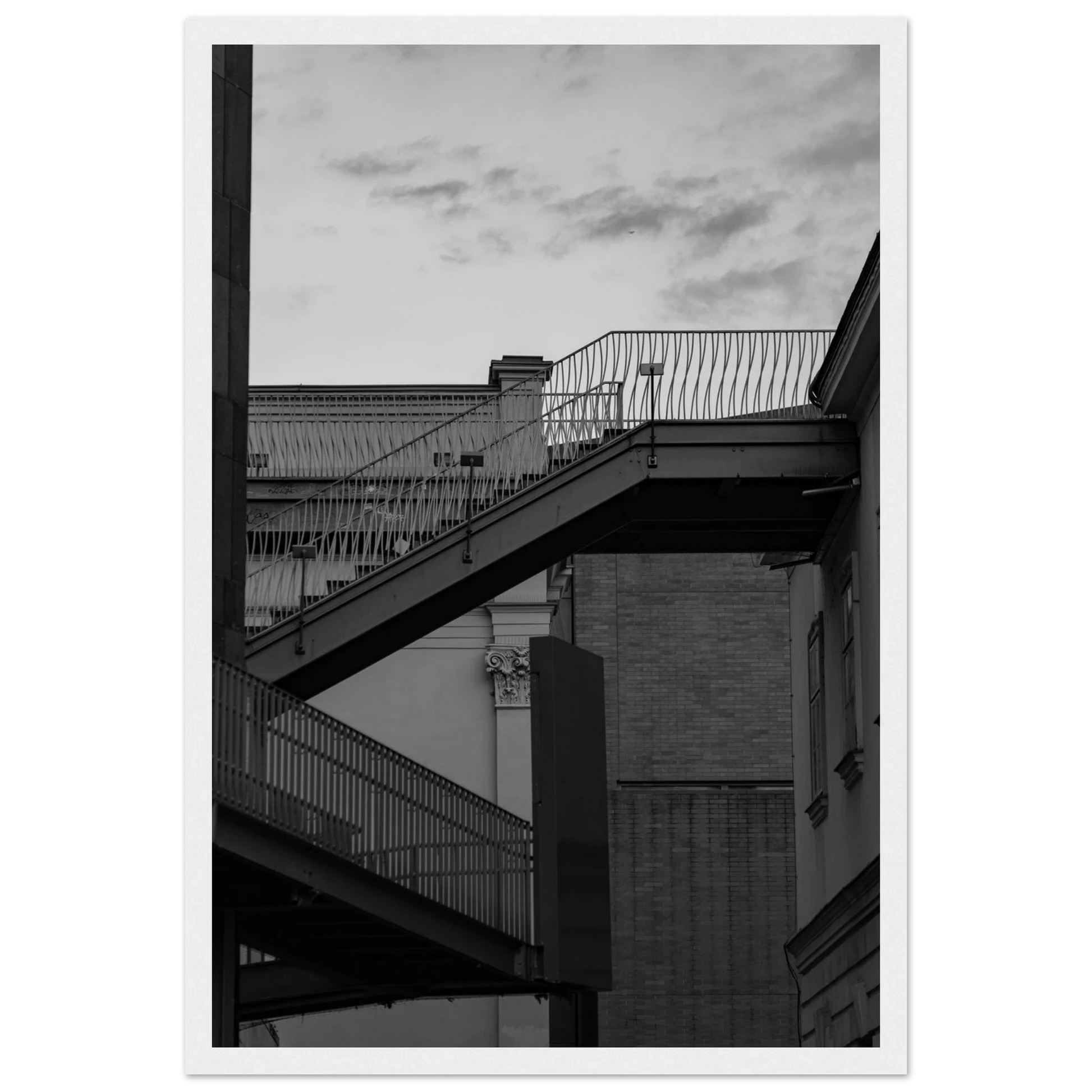 Black and white photo on a wooden frame wall art of an outdoor staircase connecting two buildings under a dramatic cloudy sky