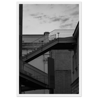 Black and white photo on a wooden frame wall art of an outdoor staircase connecting two buildings under a dramatic cloudy sky