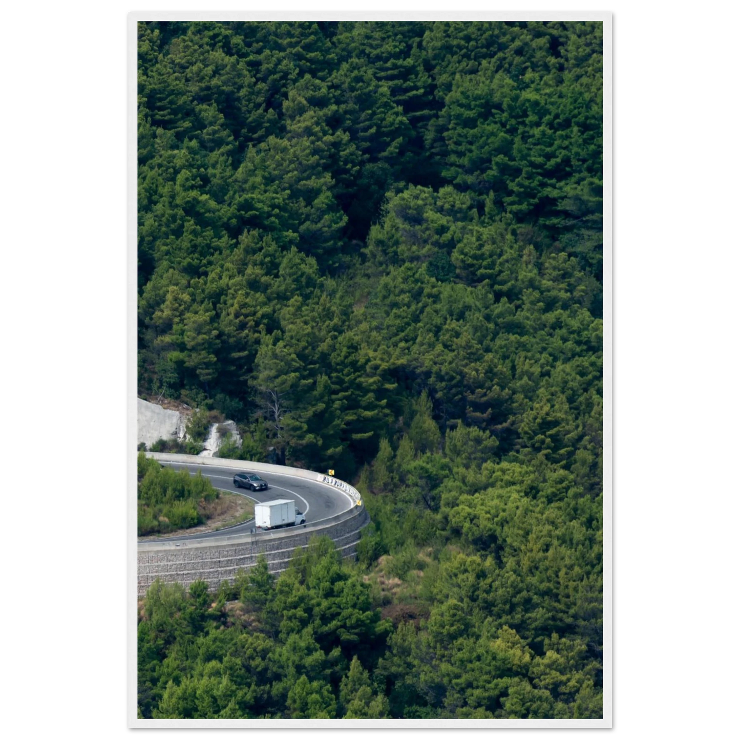 Aerial view of a winding road curve with cars surrounded by lush green forest landscape on wooden framed wall art