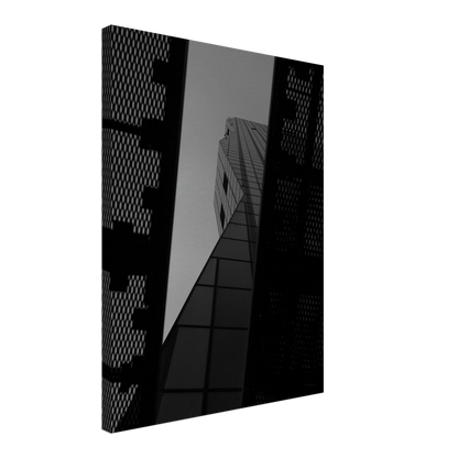 Black and white Low angle view looking up at a tall glass skyscraper framed between two metal structural elements on Canvas Print wall art