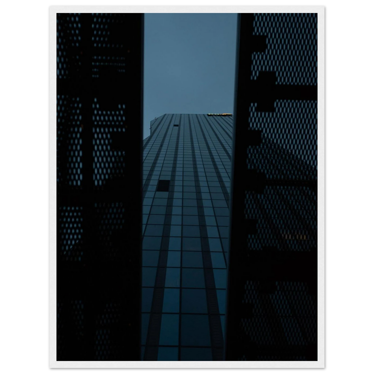 Low angle view looking up at a tall glass skyscraper framed between two metal structural elements on wooden framed wall art