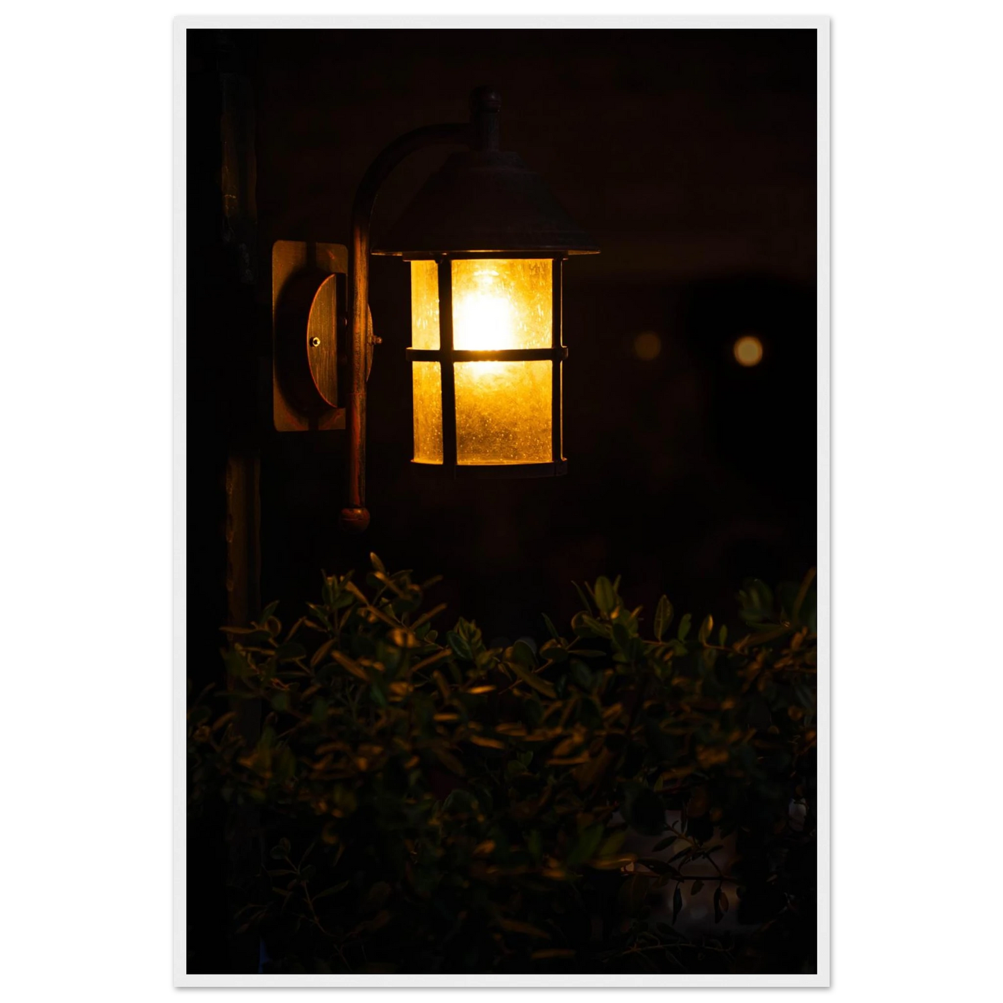 Glowing vintage lantern mounted on a wooden pole in front of a bush at night on wooden framed wall art