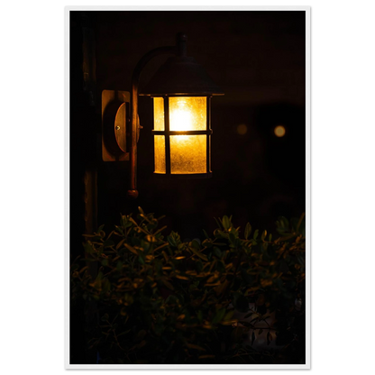 Glowing vintage lantern mounted on a wooden pole in front of a bush at night on wooden framed wall art
