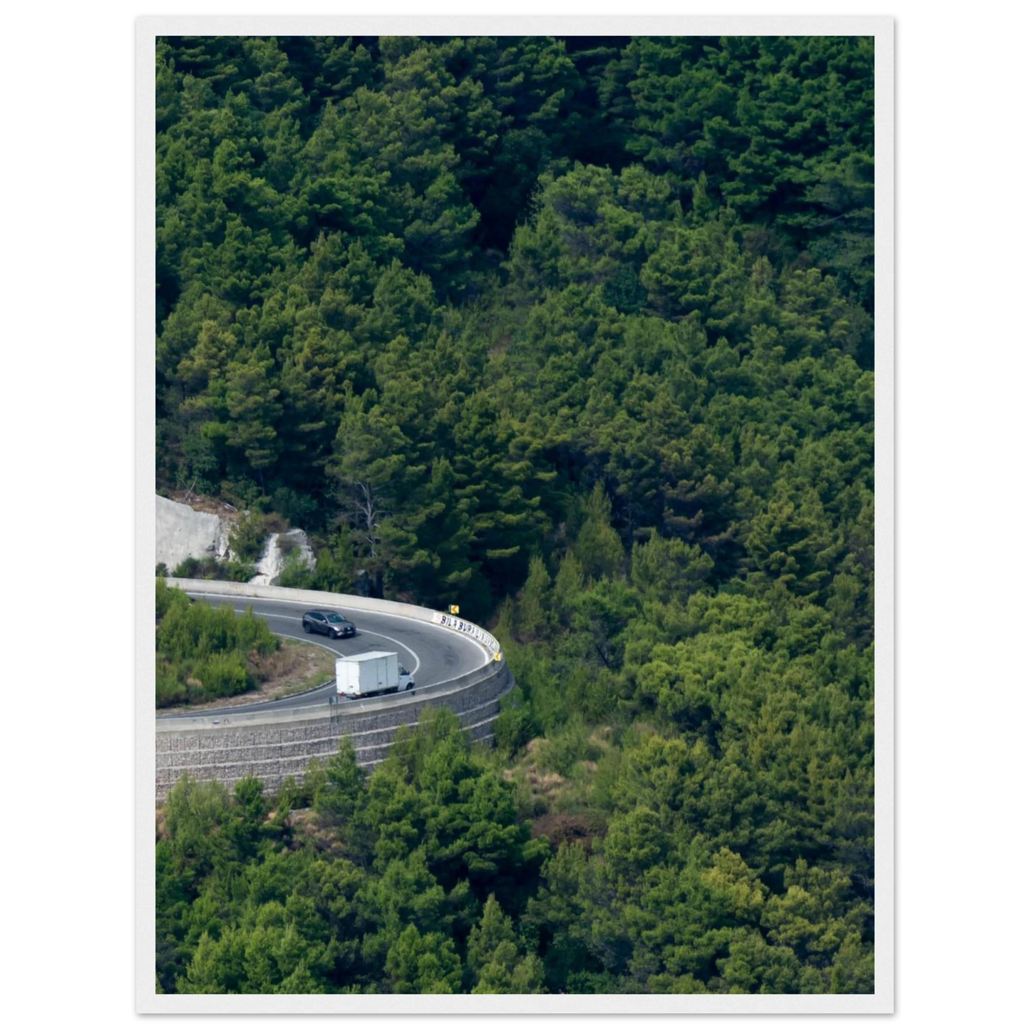 Aerial view of a winding road curve with cars surrounded by lush green forest landscape on wooden framed wall art