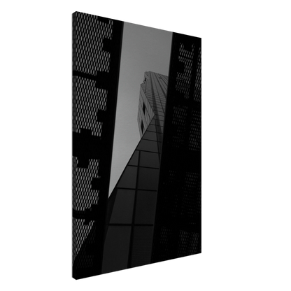 Black and white Low angle view looking up at a tall glass skyscraper framed between two metal structural elements on Canvas Print wall art