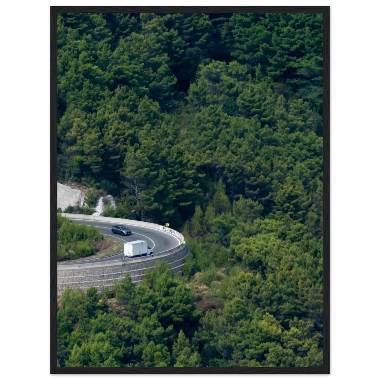 Aerial view of a winding road curve with cars surrounded by lush green forest landscape on wooden framed wall art