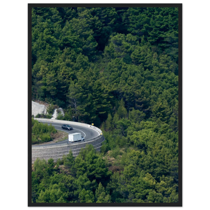 Aerial view of a winding road curve with cars surrounded by lush green forest landscape on wooden framed wall art