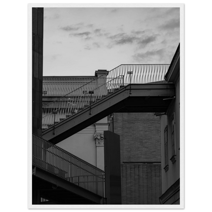 Black and white photo on a wooden frame wall art of an outdoor staircase connecting two buildings under a dramatic cloudy sky