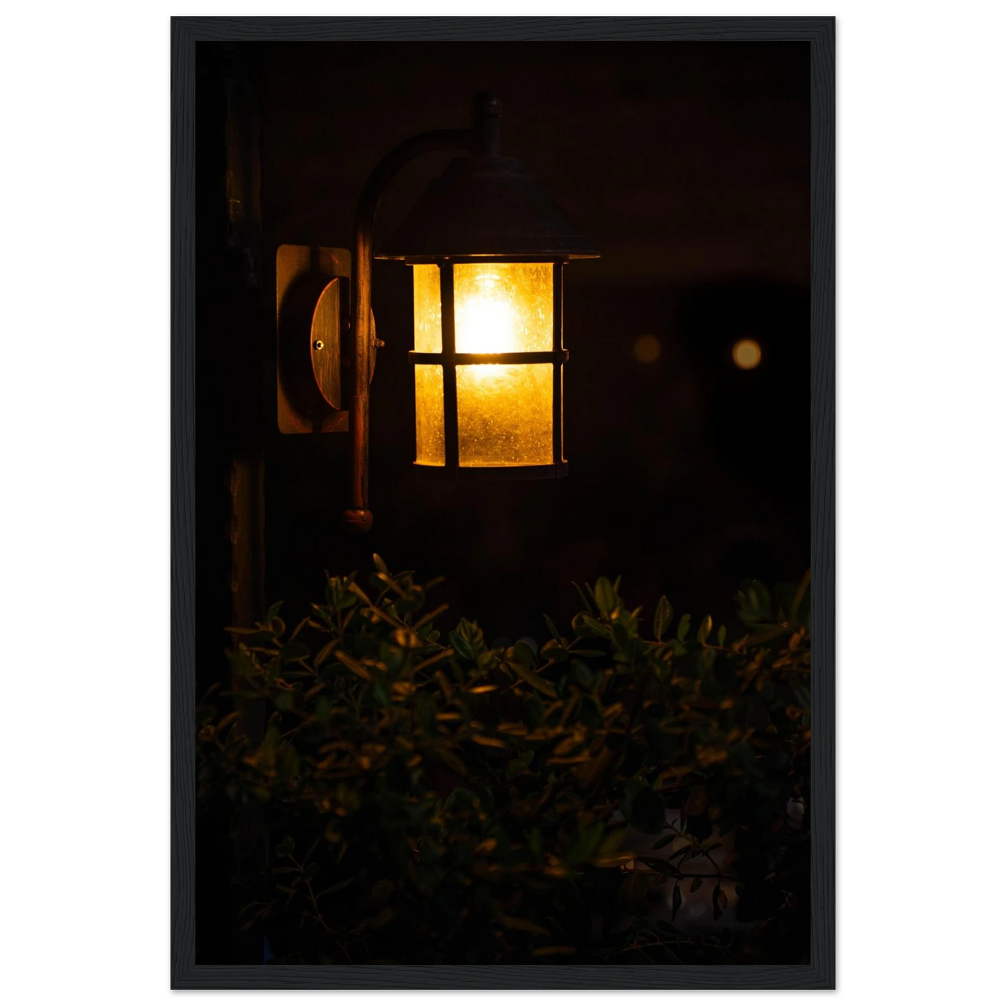 Glowing vintage lantern mounted on a wooden pole in front of a bush at night on wooden framed wall art