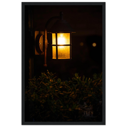 Glowing vintage lantern mounted on a wooden pole in front of a bush at night on wooden framed wall art