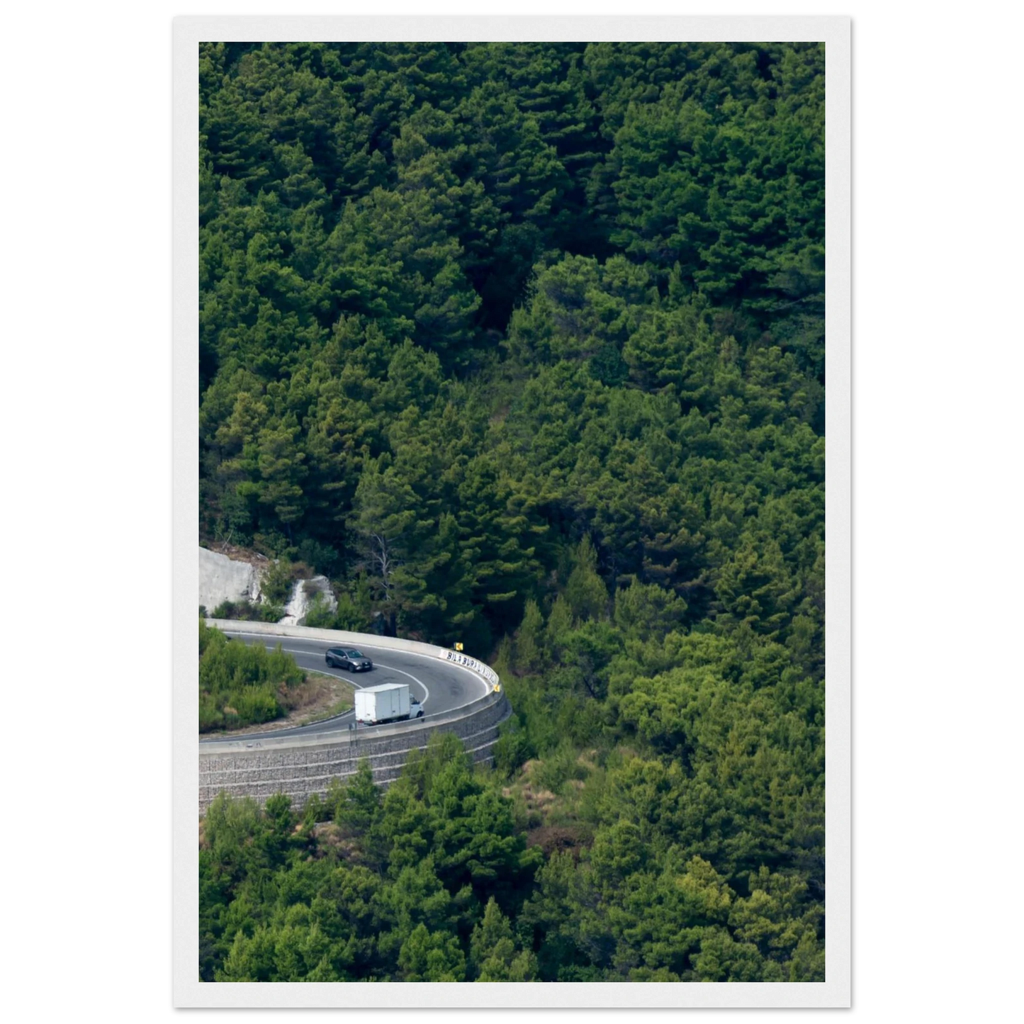 Aerial view of a winding road curve with cars surrounded by lush green forest landscape on wooden framed wall art