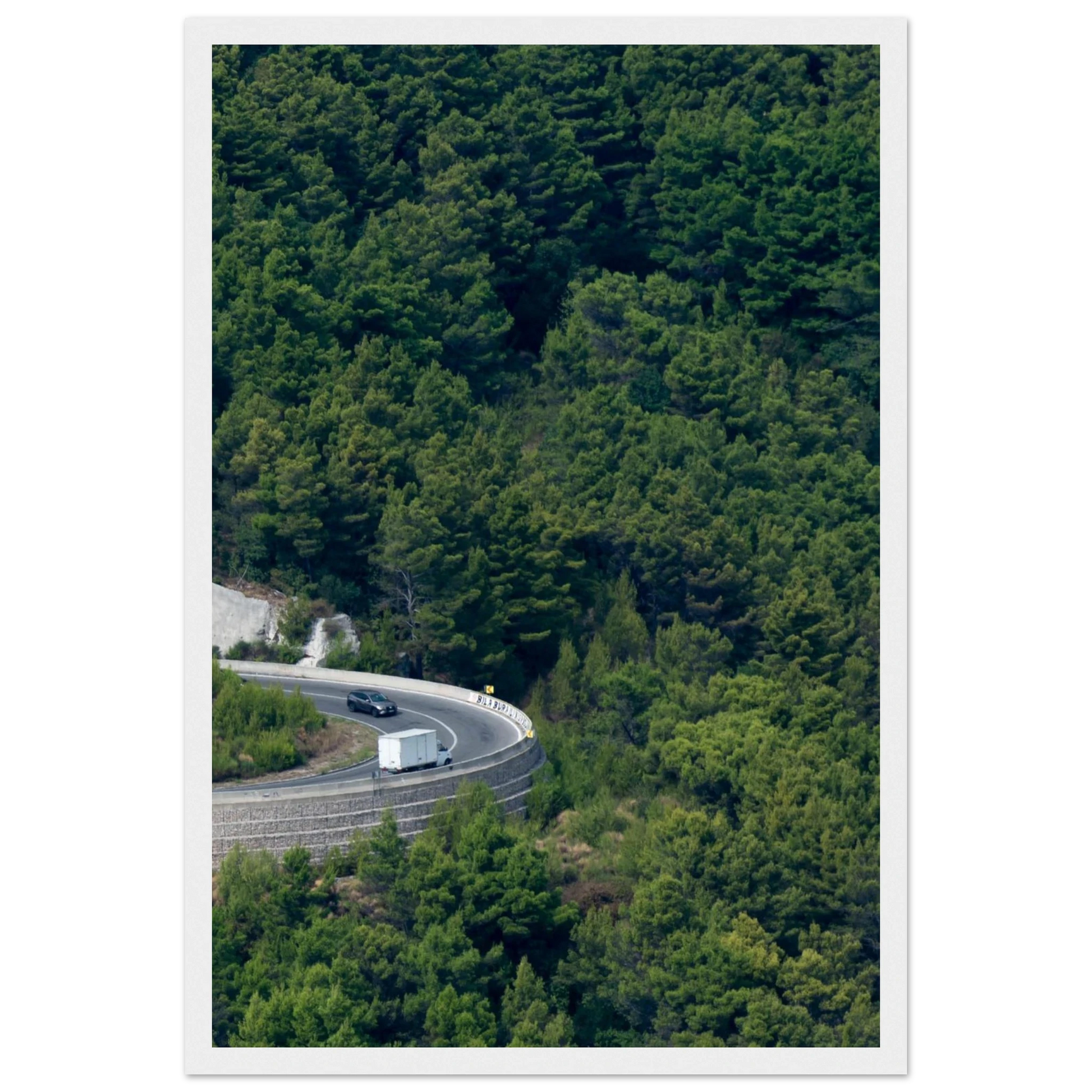 Aerial view of a winding road curve with cars surrounded by lush green forest landscape on wooden framed wall art
