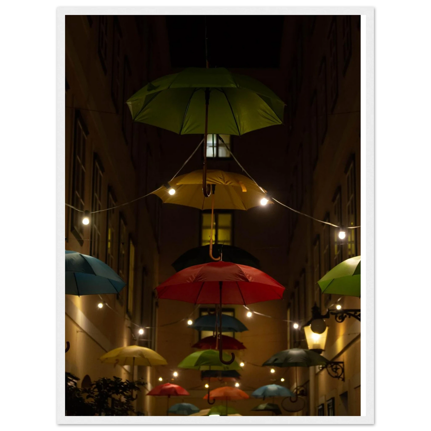 Nighttime street scene with colorful illuminated umbrellas hanging as decoration above a vibrant outdoor area on a wooden frame wall art
