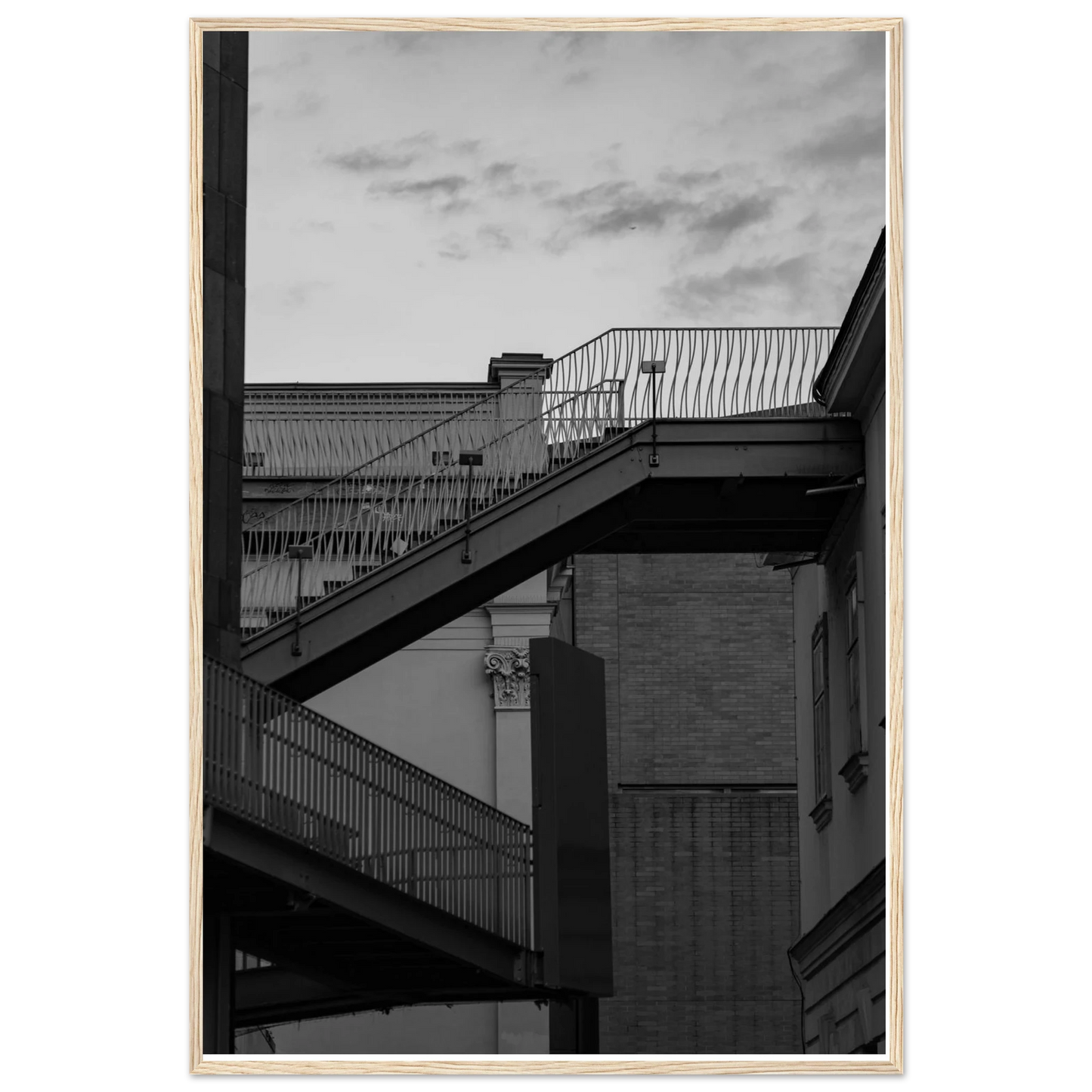 Black and white photo on a wooden frame wall art of an outdoor staircase connecting two buildings under a dramatic cloudy sky