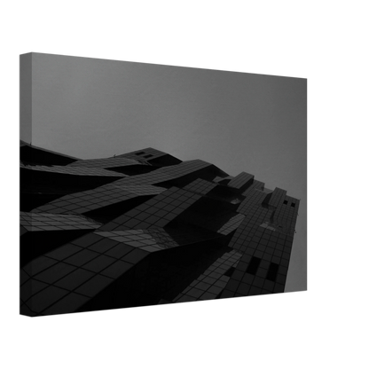Black and white low angle view of a modern skyscraper with bold geometric lines and dark textured facade on Canvas Print wall art