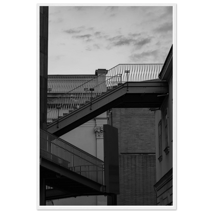 Black and white photo on a wooden frame wall art of an outdoor staircase connecting two buildings under a dramatic cloudy sky
