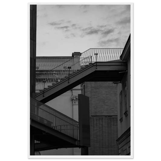 Black and white photo on a wooden frame wall art of an outdoor staircase connecting two buildings under a dramatic cloudy sky