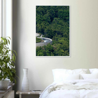 Aerial view of a winding road curve with cars surrounded by lush green forest landscape on wooden framed wall art on the wall in the Bedroom