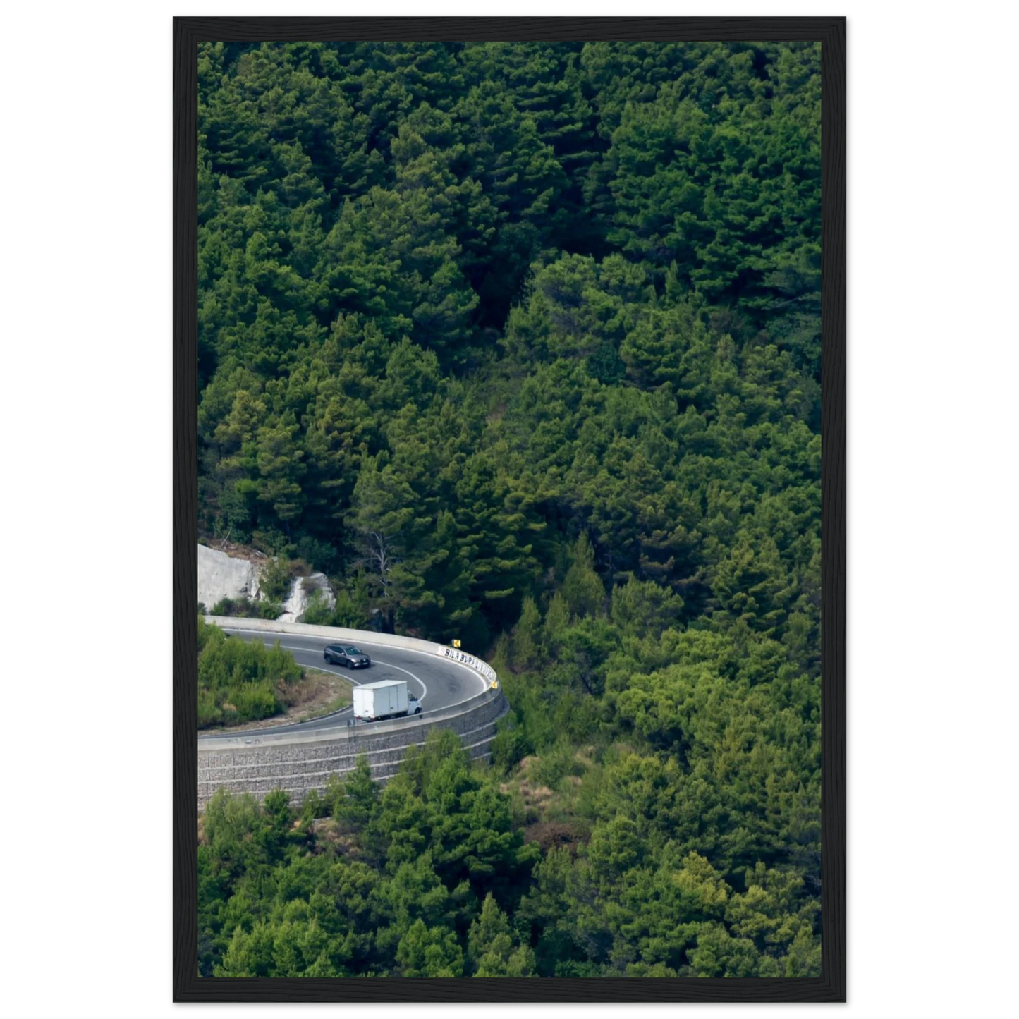 Aerial view of a winding road curve with cars surrounded by lush green forest landscape on wooden framed wall art