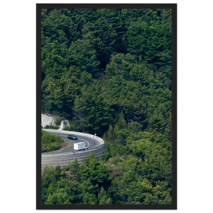 Aerial view of a winding road curve with cars surrounded by lush green forest landscape on wooden framed wall art