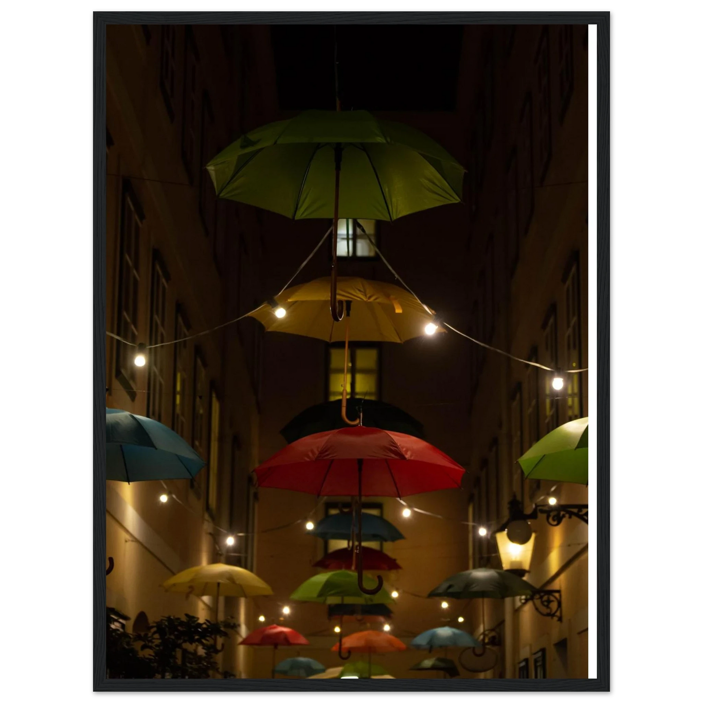 Nighttime street scene with colorful illuminated umbrellas hanging as decoration above a vibrant outdoor area on a wooden frame wall art