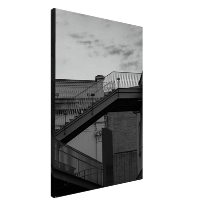 Black and white photo on a Canvas Print wall art of an outdoor staircase connecting two buildings under a dramatic cloudy sky
