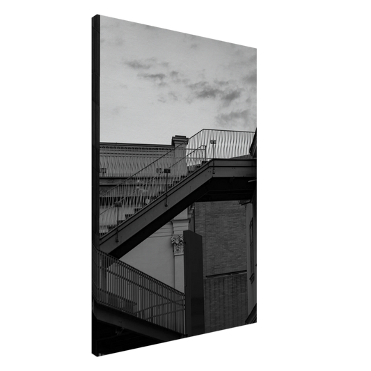 Black and white photo on a Canvas Print wall art of an outdoor staircase connecting two buildings under a dramatic cloudy sky