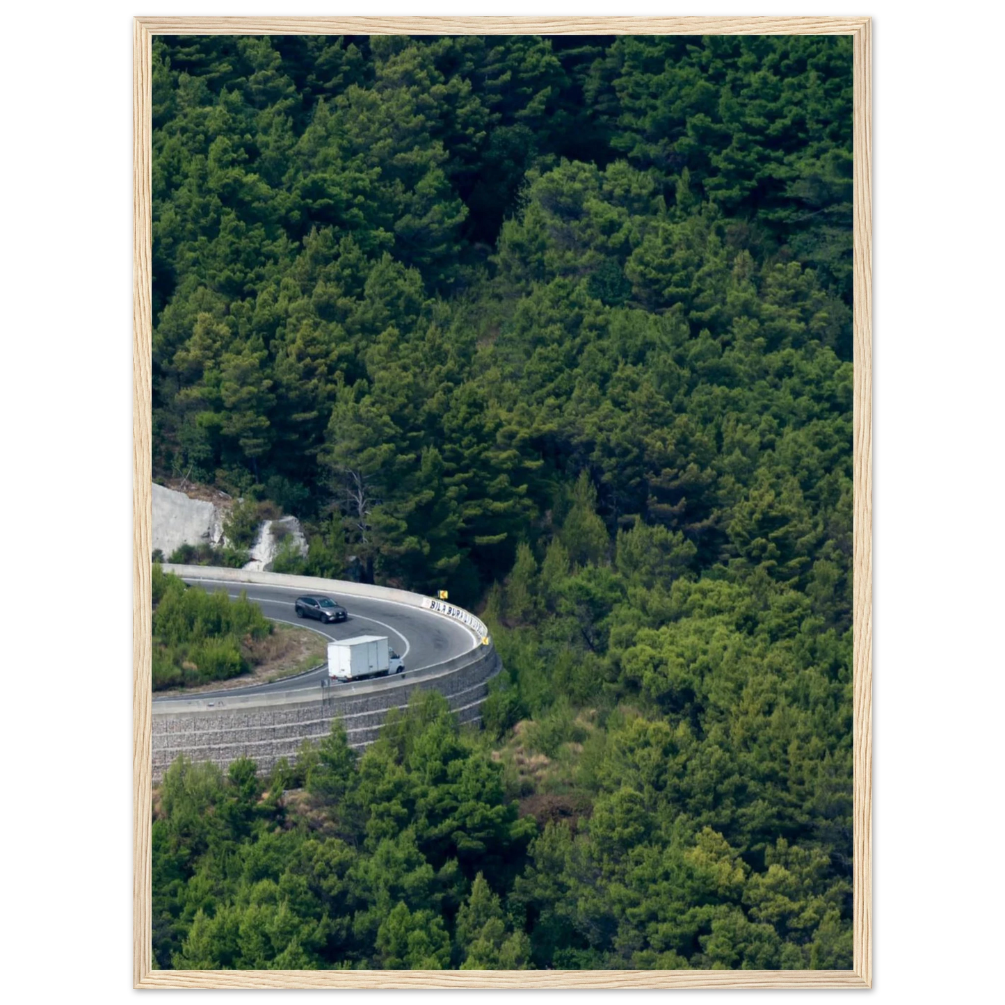 Aerial view of a winding road curve with cars surrounded by lush green forest landscape on wooden framed wall art