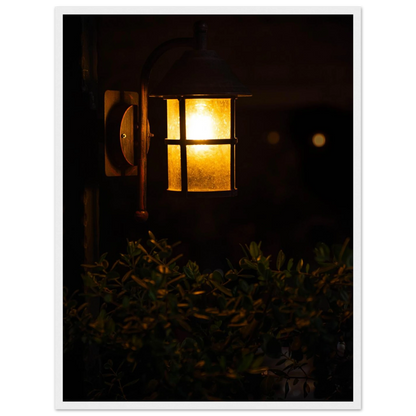 Glowing vintage lantern mounted on a wooden pole in front of a bush at night on wooden framed wall art