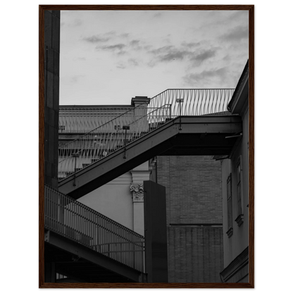 Black and white photo on a wooden frame wall art of an outdoor staircase connecting two buildings under a dramatic cloudy sky
