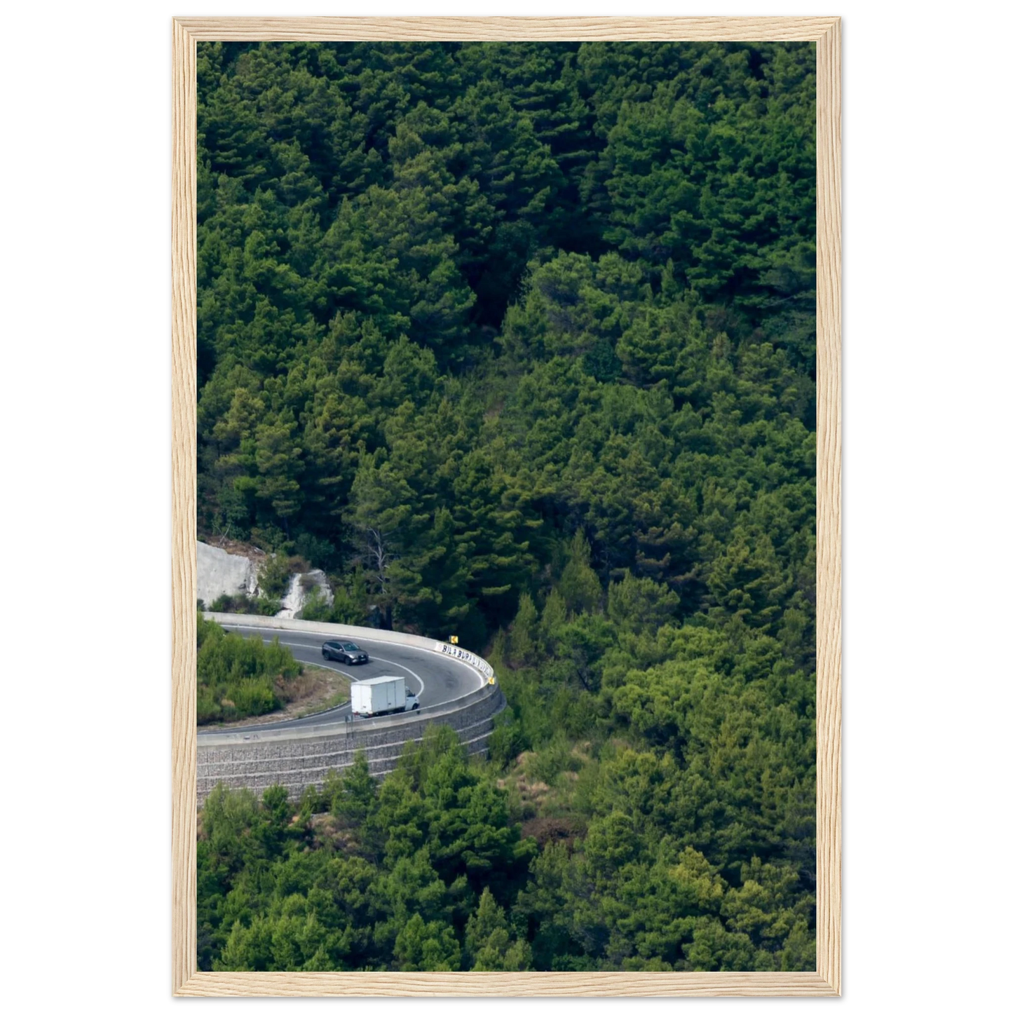Aerial view of a winding road curve with cars surrounded by lush green forest landscape on wooden framed wall art