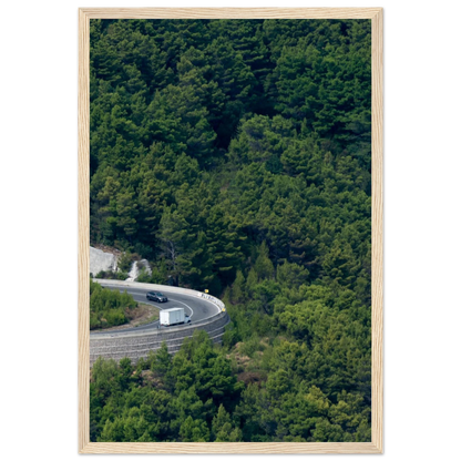 Aerial view of a winding road curve with cars surrounded by lush green forest landscape on wooden framed wall art