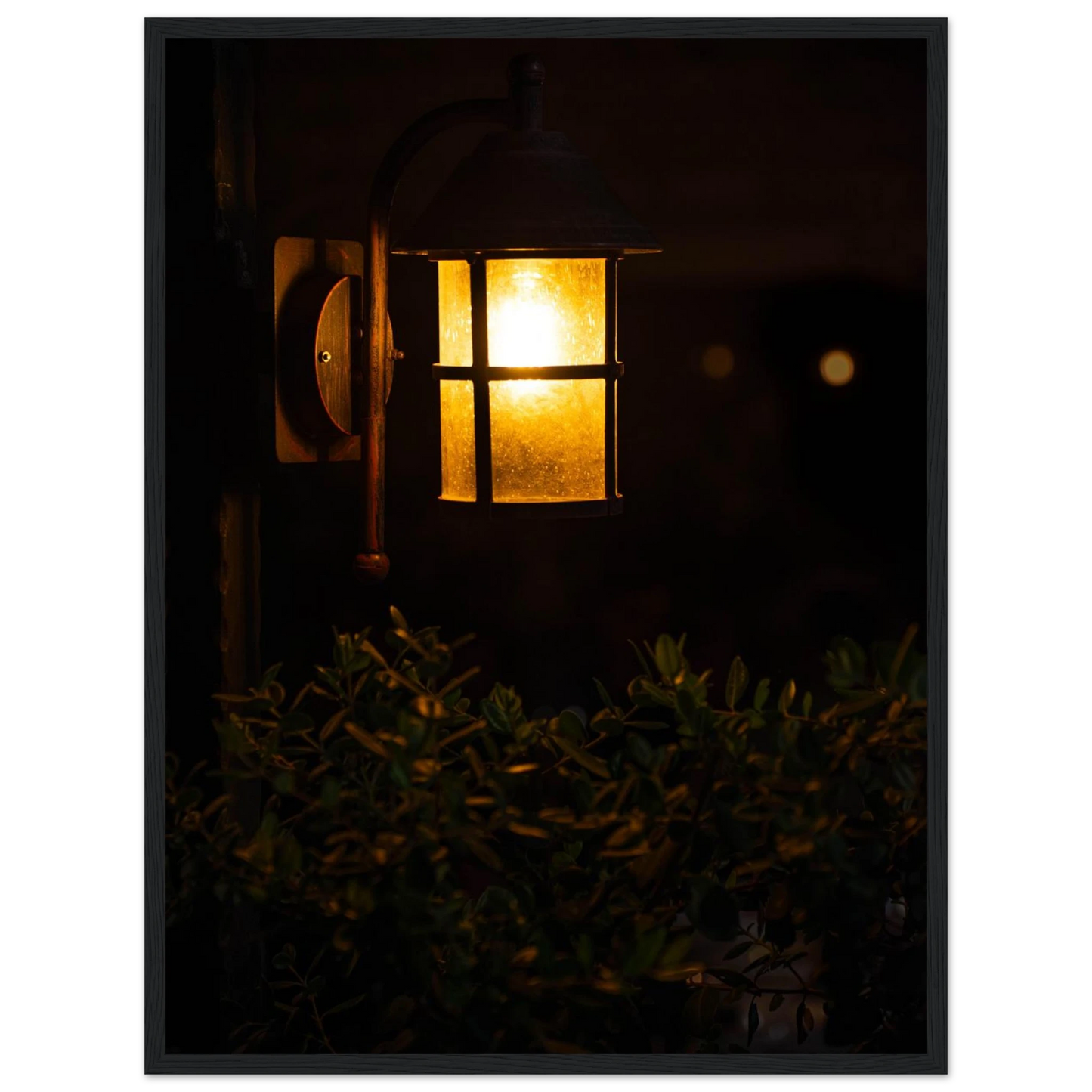 Glowing vintage lantern mounted on a wooden pole in front of a bush at night on wooden framed wall art