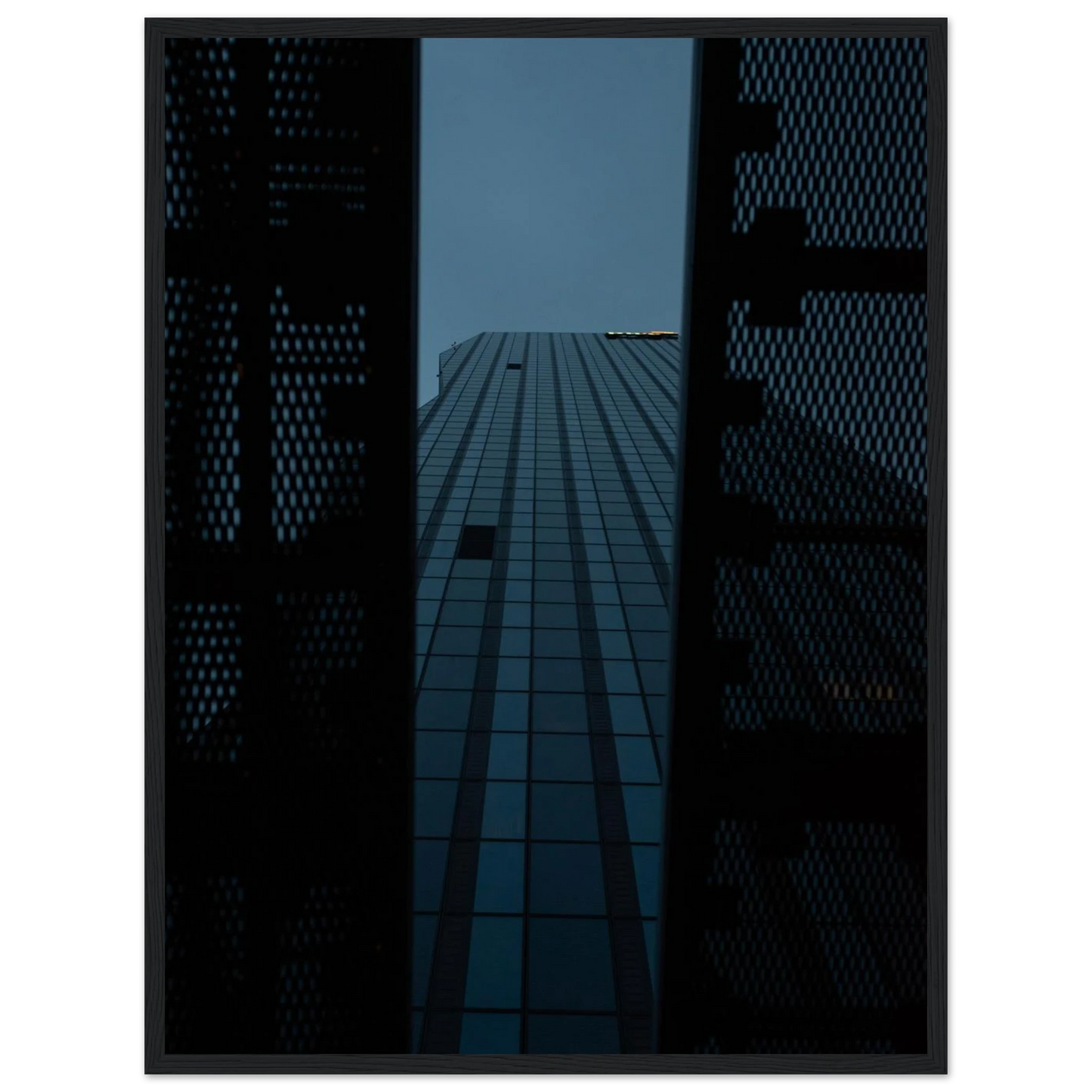 Low angle view looking up at a tall glass skyscraper framed between two metal structural elements on wooden framed wall art