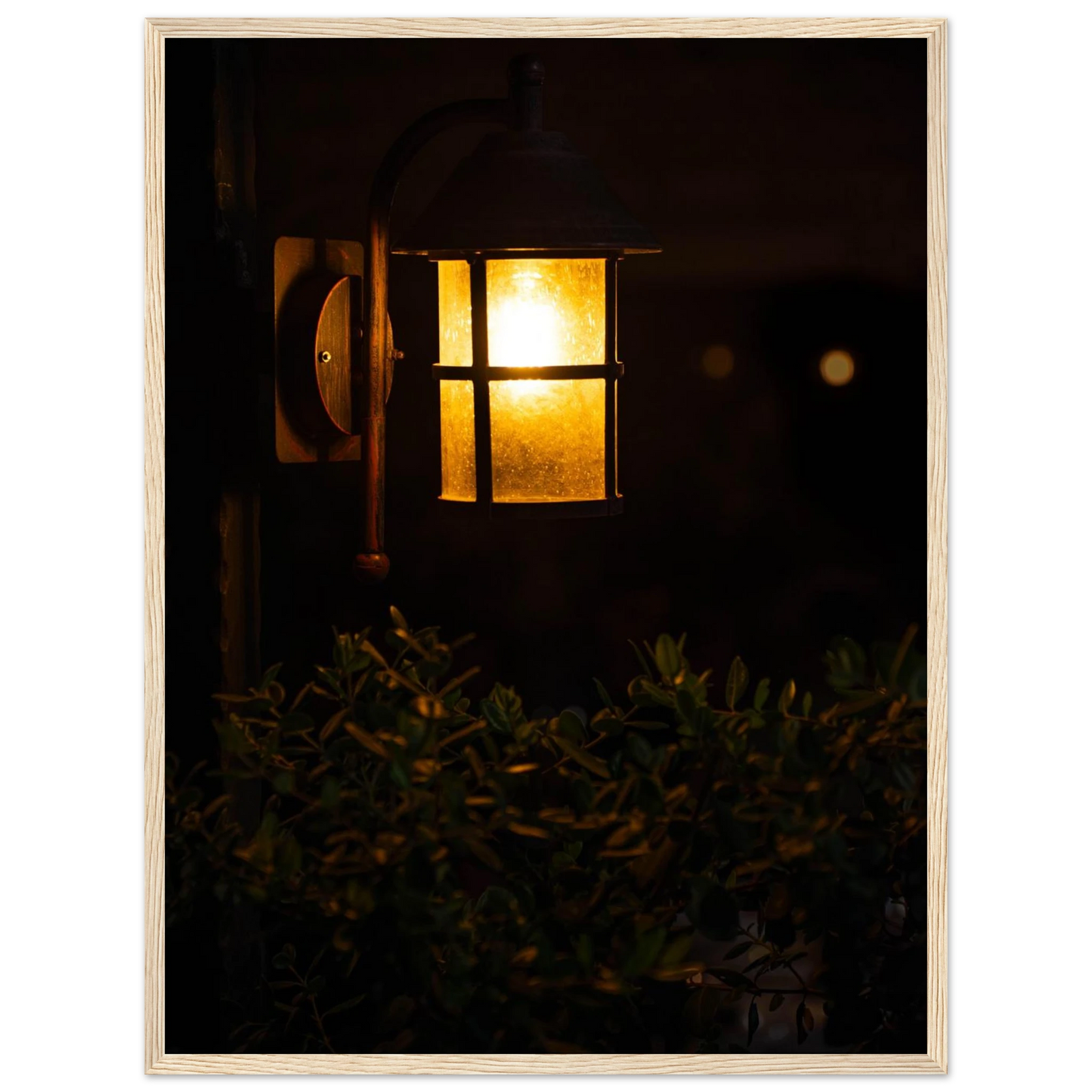 Glowing vintage lantern mounted on a wooden pole in front of a bush at night on wooden framed wall art