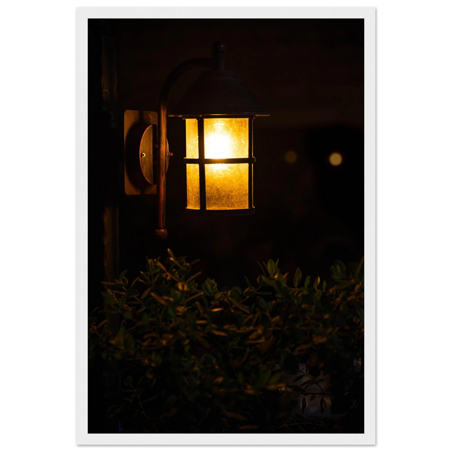 Glowing vintage lantern mounted on a wooden pole in front of a bush at night on wooden framed wall art